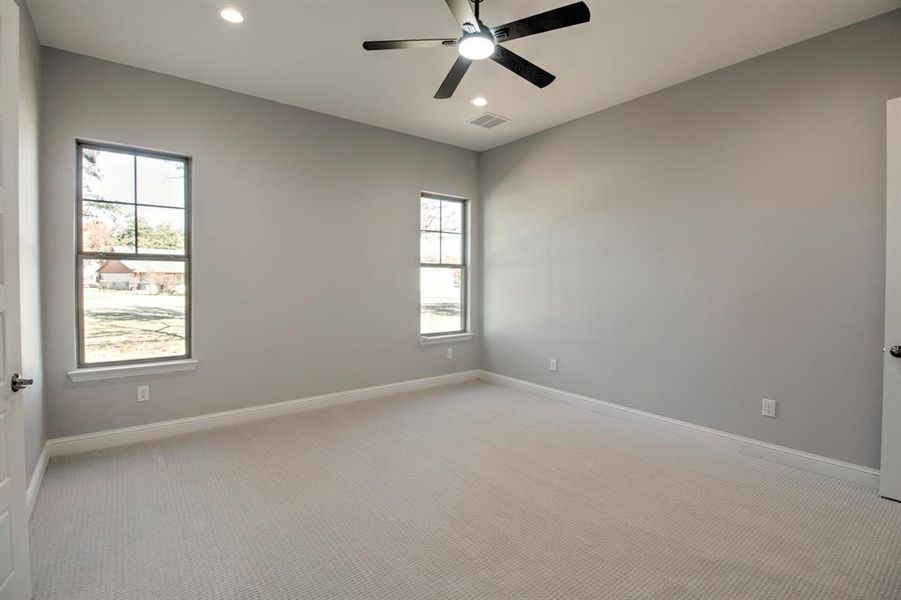 Empty room with ceiling fan, light carpet, and a wealth of natural light