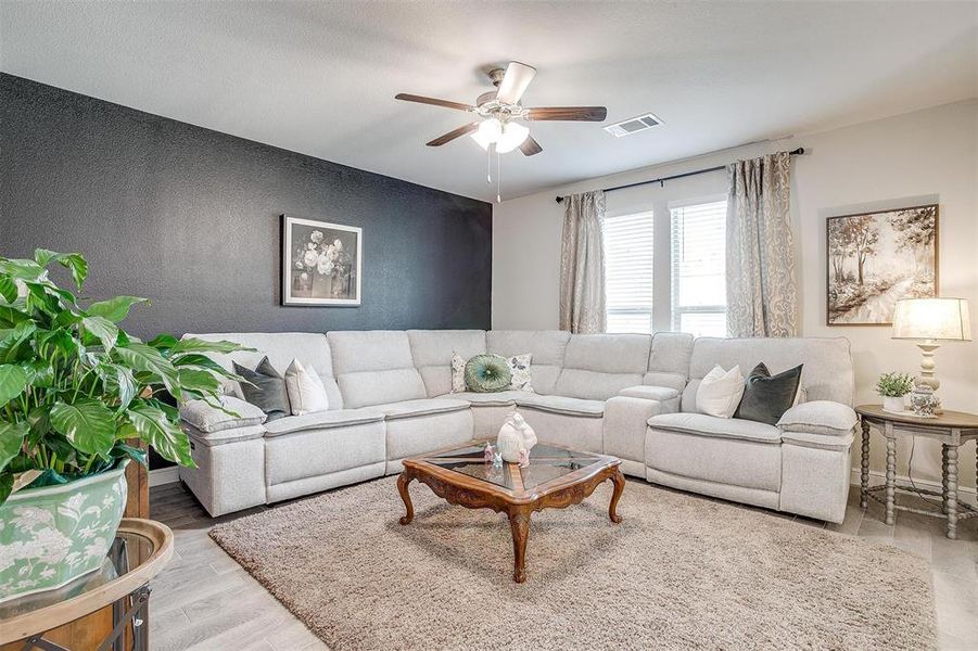 Living room featuring an accent wall, wood finished floors, visible vents, baseboards, and a ceiling fan