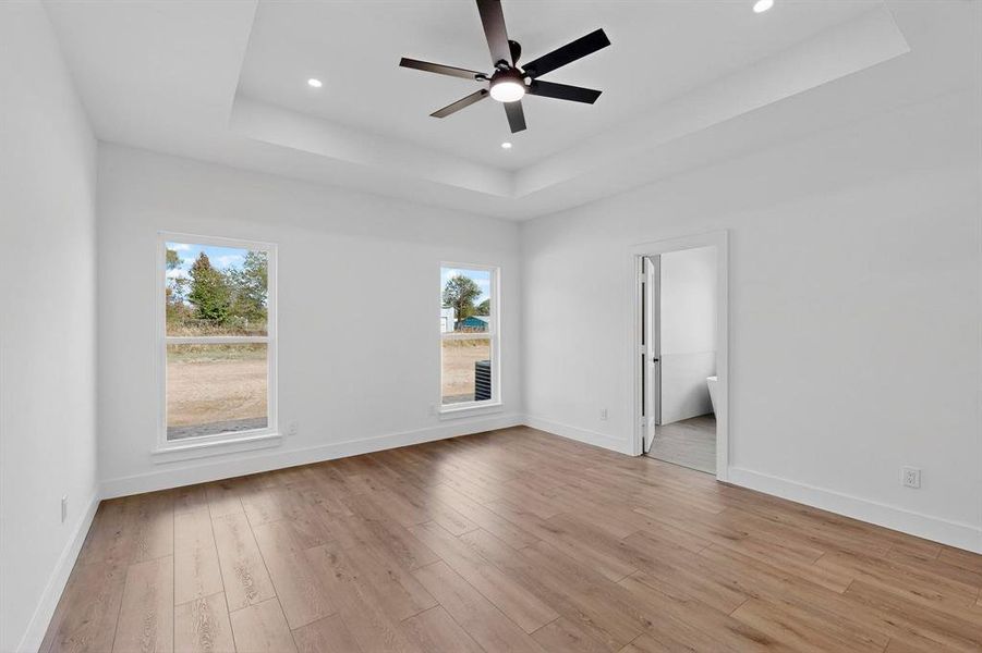 Unfurnished bedroom featuring a raised ceiling, light wood-style floors, ceiling fan, and recessed lighting