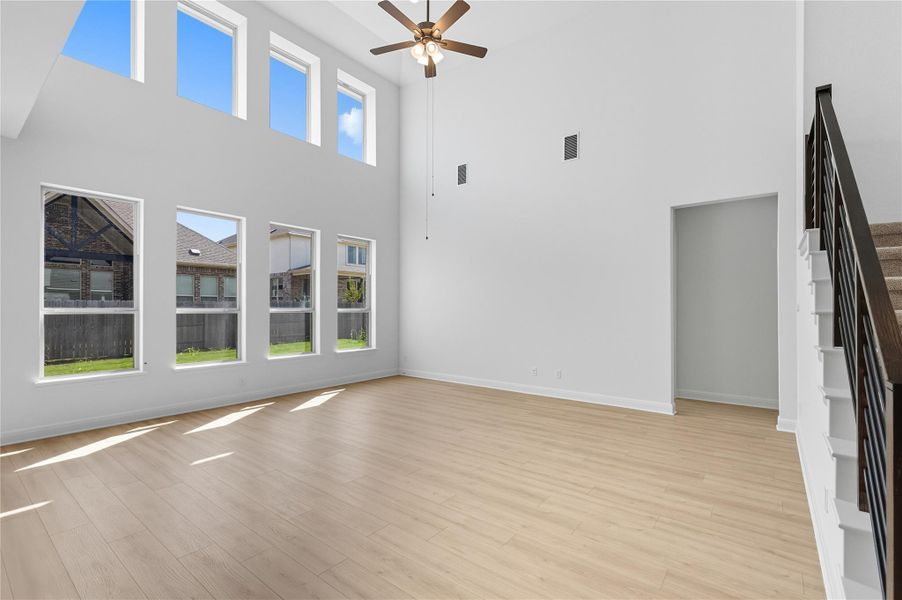 Unfurnished living room featuring stairs, light wood-type flooring, a ceiling fan, and a high ceiling