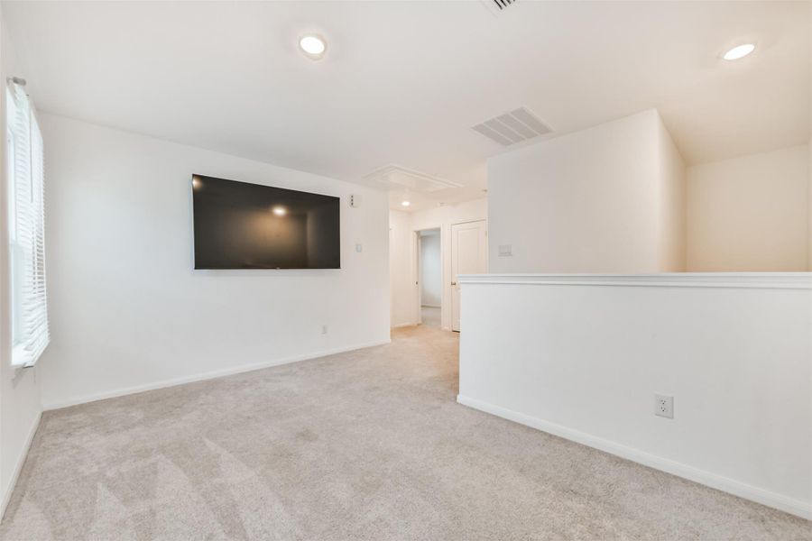 The gameroom features a cozy, carpeted space with neutral walls and ample natural light. It's ideal for a media or relaxation area. *The TV will be removed but the wall mount will stay*