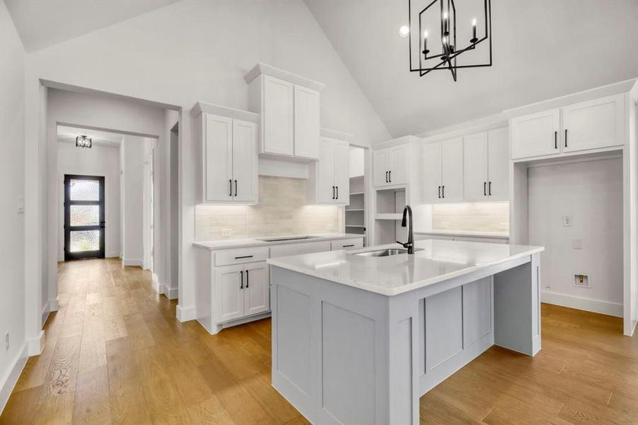 Kitchen with white cabinetry, a kitchen island with sink, lofted ceiling, light stone countertops, and light wood-style flooring