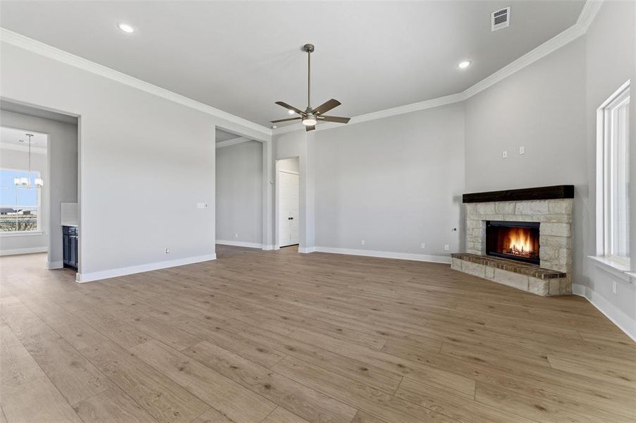 Unfurnished living room with a stone fireplace, light wood-style floors, ornamental molding, a ceiling fan, and recessed lighting