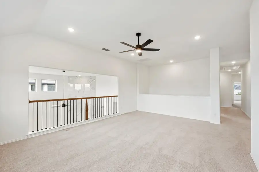 Open upstairs loft with carpet flooring, ceiling fan, and iron stair railing overlooking lower level
