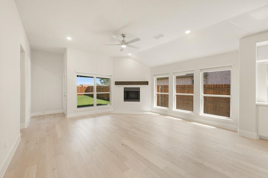 Empty living room with light hardwood floors, fireplace, vaulted ceiling, ceiling fan, and large windows