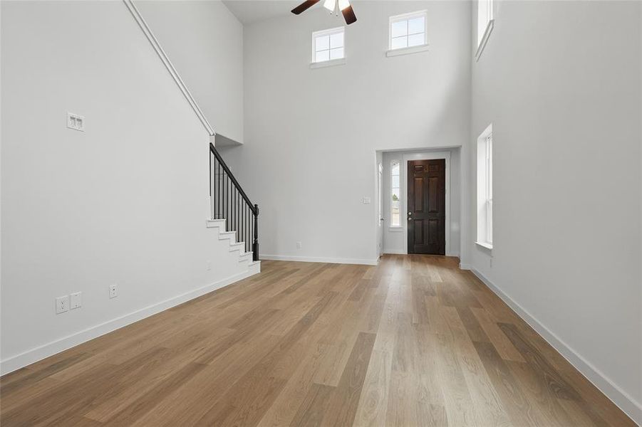 Entryway featuring stairway, a ceiling fan, a towering ceiling, light wood-style floors, and baseboards Entryway featuring stairway, a ceiling fan, a towering ceiling, light wood-style floors, and baseboards
