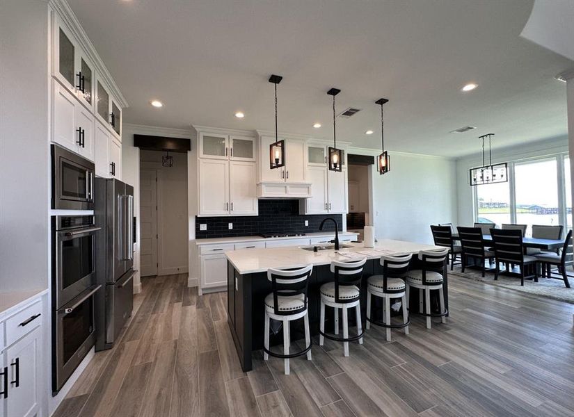 Kitchen featuring stainless steel appliances, backsplash, dark wood-style flooring, a kitchen bar, and recessed lighting Kitchen featuring stainless steel appliances, backsplash, dark wood-style flooring, a kitchen bar, and recessed lighting