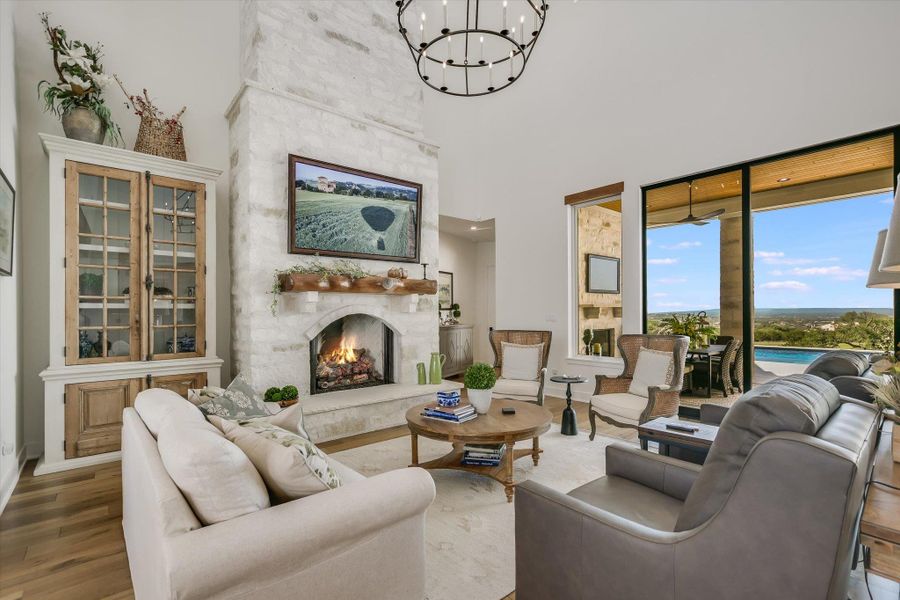 Living area with a chandelier, wood finished floors, a large fireplace, a towering ceiling, and baseboards Living area with a chandelier, wood finished floors, a large fireplace, a towering ceiling, and baseboards