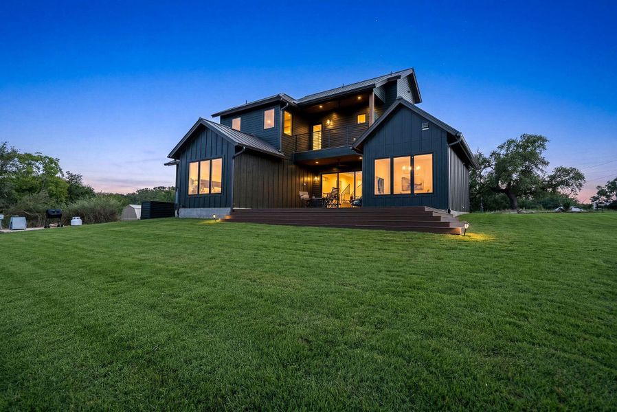 A spacious green lawn sits behind this modern dark siding home under twilight skies.