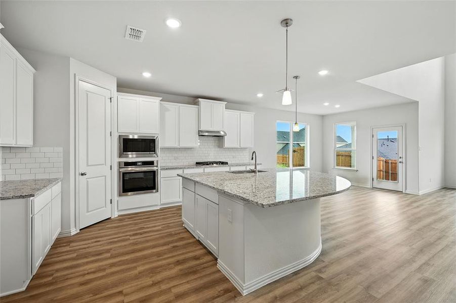 Kitchen with hanging light fixtures, white cabinetry, light stone countertops, a center island with sink, and recessed lighting Kitchen with hanging light fixtures, white cabinetry, light stone countertops, a center island with sink, and recessed lighting