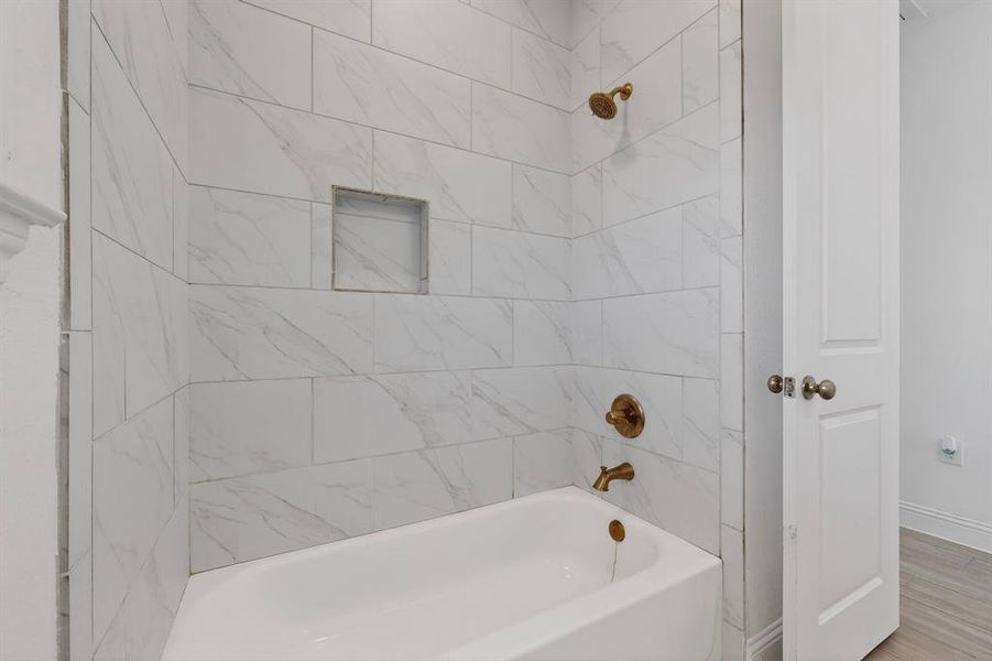 Bathtub shower combination featuring marble-look tile surround with a built-in niche, and brass fixtures Bathtub shower combination featuring marble-look tile surround with a built-in niche, and brass fixtures