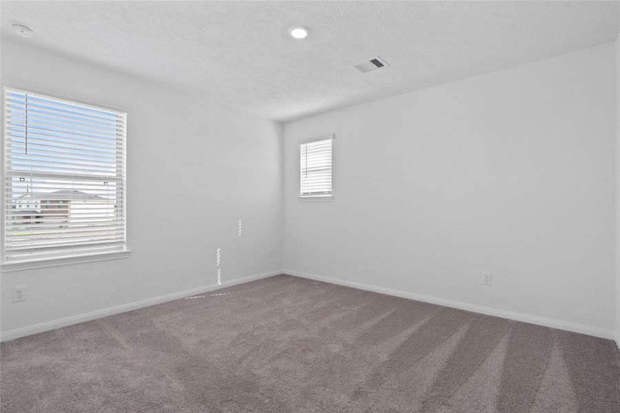 This secondary bedroom offers comfort and style with plush carpeting, neutral paint tones, recessed lighting, large window, and a walk-in closet.