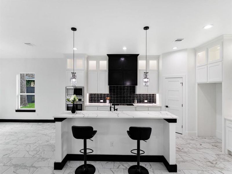 Spacious kitchen featuring an island with a light-toned countertop, recessed lighting, white cabinetry with glass-front uppers, a dark tile backsplash, and stainless steel appliances