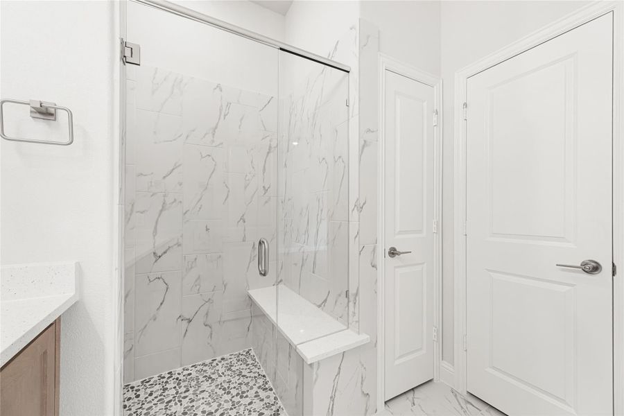 Walk-in shower with marble tile walls, built-in bench, glass door, and pebble stone floor Walk-in shower with marble tile walls, built-in bench, glass door, and pebble stone floor