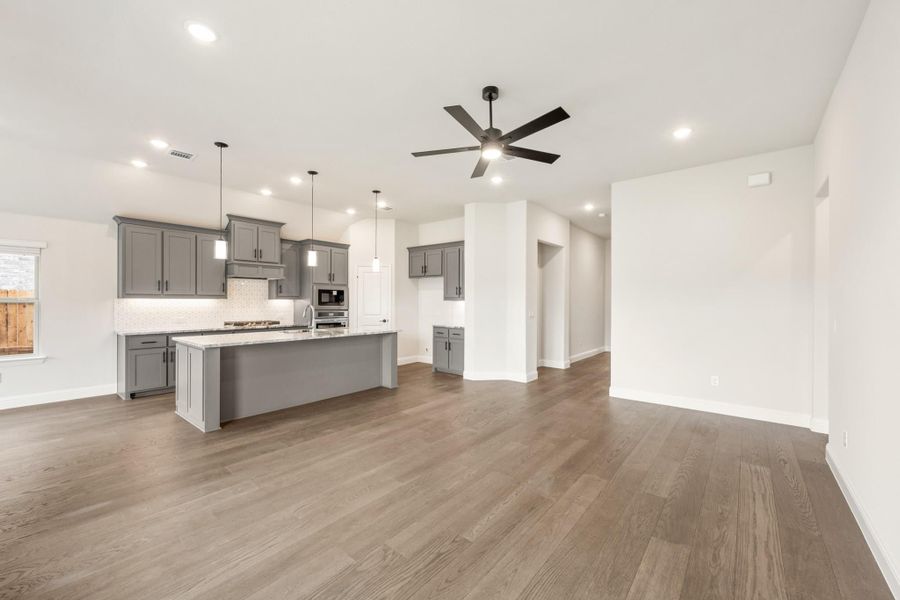 Open-concept kitchen and living area with gray cabinets, large island, hardwood floors, and ceiling fan Open-concept kitchen and living area with gray cabinets, large island, hardwood floors, and ceiling fan