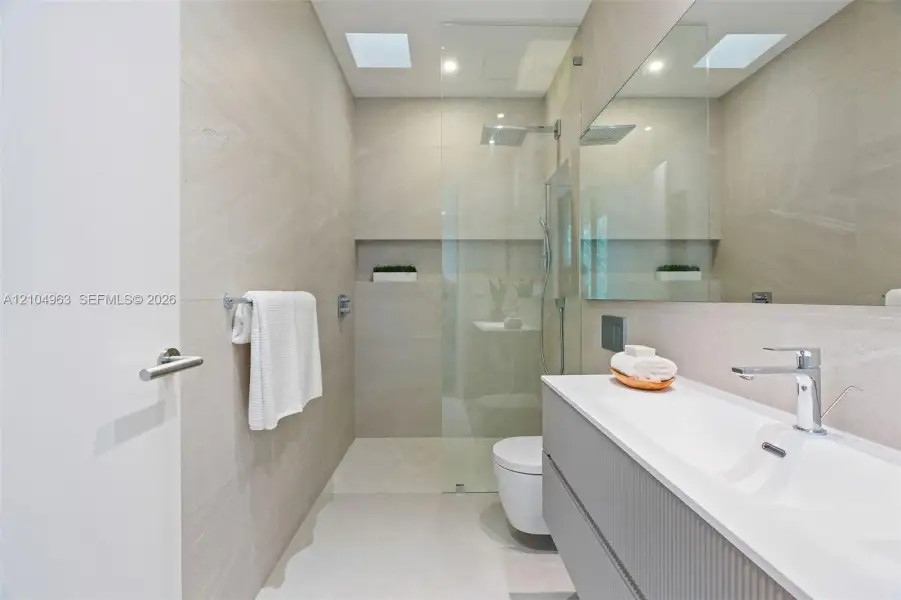 Modern bathroom featuring floor-to-ceiling textured wall tiling, a floating vanity with a seamless integrated sink, a glass-enclosed shower with a built-in recessed wall niche, and a large wall-to-wall mirror