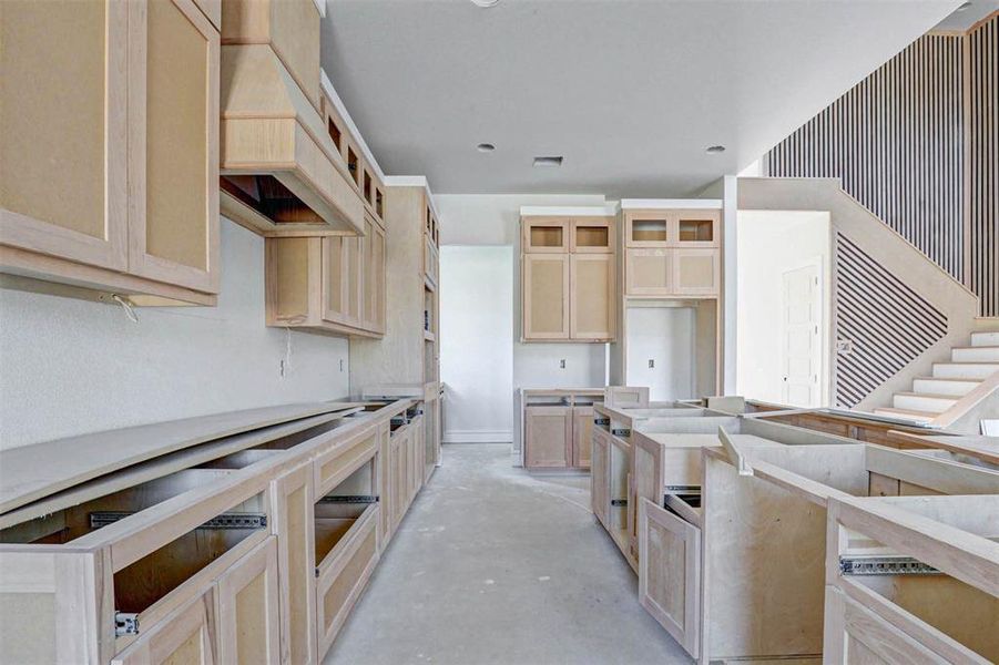 Kitchen with light brown cabinetry and custom exhaust hood