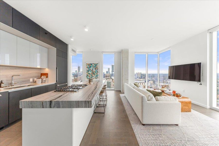 A designer kitchen anchored by upgraded Fantasy Ocean marble countertops and custom cabinetry, connecting directly to a light-filled living space with sweeping skyline vistas. A designer kitchen anchored by upgraded Fantasy Ocean marble countertops and custom cabinetry, connecting directly to a light-filled living space with sweeping skyline vistas.