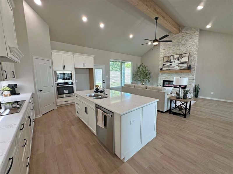 Kitchen featuring white cabinetry, beamed ceiling, light wood-type flooring, stainless steel appliances, and high vaulted ceiling Kitchen featuring white cabinetry, beamed ceiling, light wood-type flooring, stainless steel appliances, and high vaulted ceiling