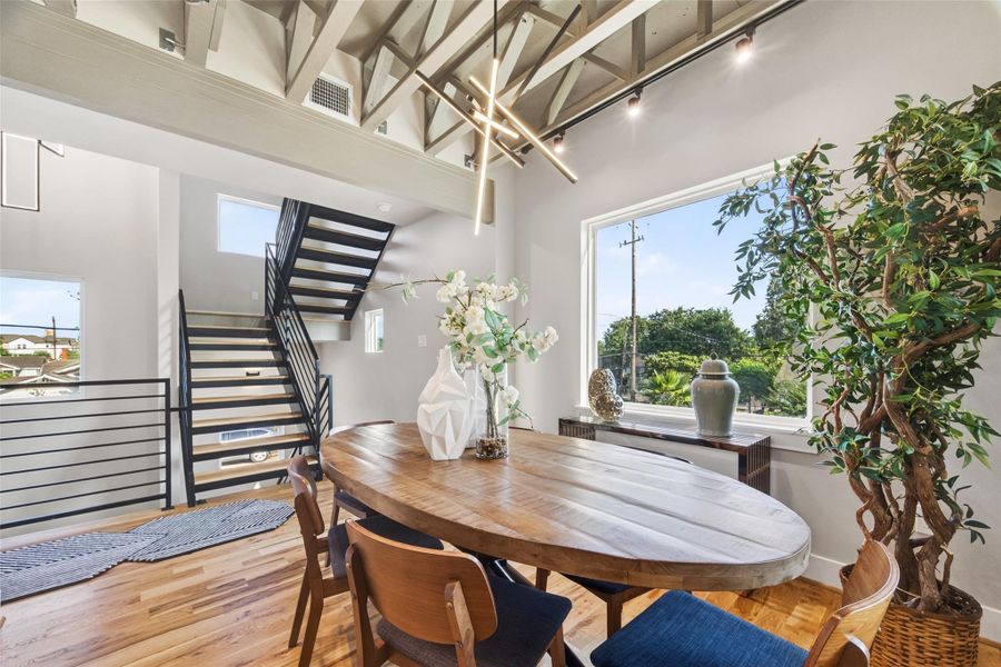 Dramatic exposed structural trusses define the second-floor dining space, adding an industrial-chic character rarely found in new construction. A large picture window frames the treeline, and a modern pendant light fixture centers the room, an inviting backdrop for everyday meals and entertaining alike.