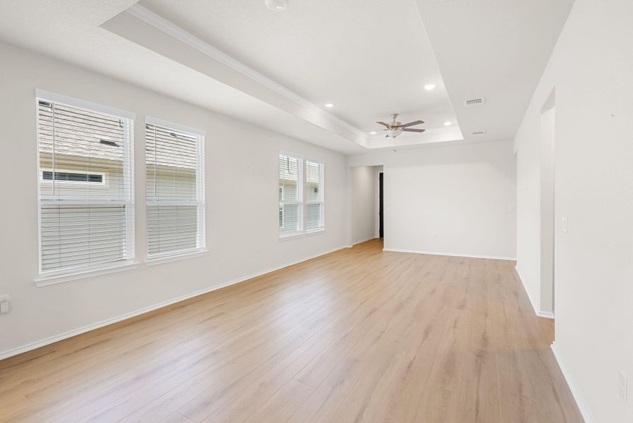 A luminous living space features light wood flooring and a recessed tray ceiling with modern lighting. A luminous living space features light wood flooring and a recessed tray ceiling with modern lighting.