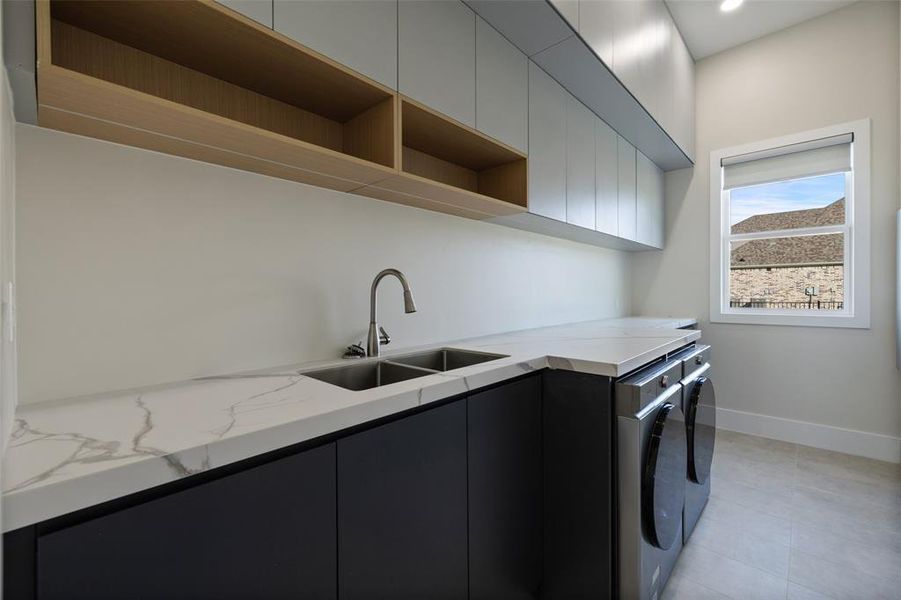 Clothes washing area with cabinets, washer and dryer, sink, and light tile patterned floors