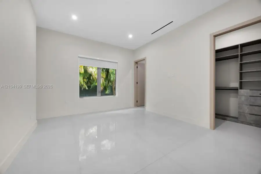 Neutral-toned interior featuring large-format tile flooring, recessed lighting, and a walk-in closet equipped with custom built-in shelving and drawers