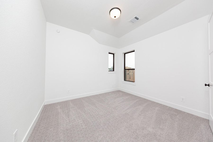 This secondary bedroom features a sloped ceiling, plush carpet flooring, windows, a walk-in closet.