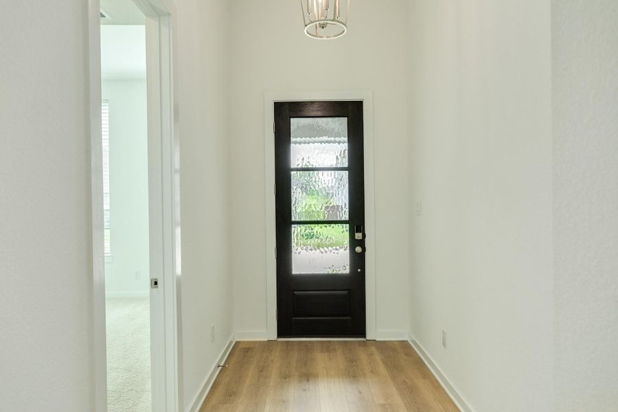 Upon entering the home, you are greeted by stunning engineered hardwood floors. To the right, you will find a spacious guest bedroom accompanied by a full bathroom; to the left, you will find the entrance to the garage and laundry area.