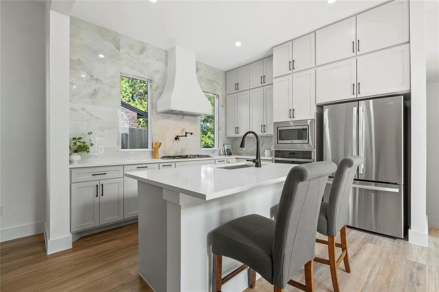 Kitchen featuring stainless steel appliances, a breakfast bar, a center island with sink, backsplash, and light wood-style flooring