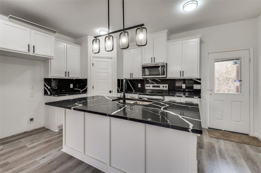 Kitchen with backsplash, stainless steel appliances, pendant lighting, a center island with sink, and light hardwood / wood-style floors