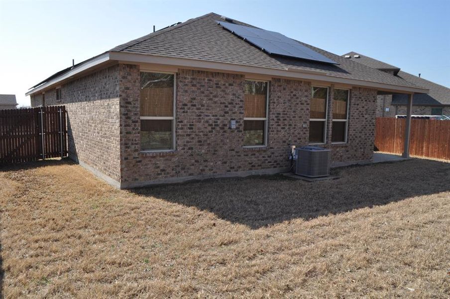 Rear view of house with a yard, solar panels, and central air condition unit