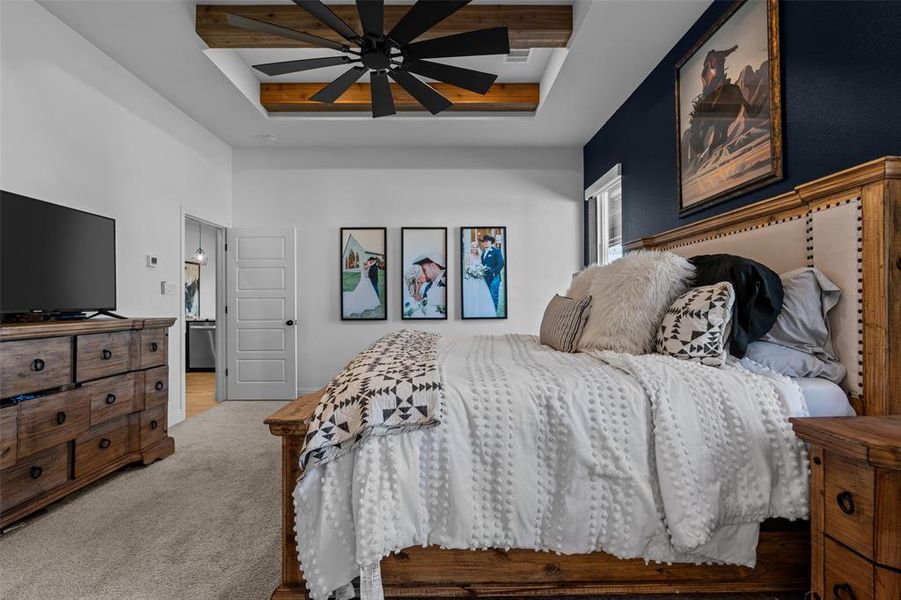 Bedroom featuring light carpet, ensuite bath, a raised ceiling, ceiling fan, and beam ceiling