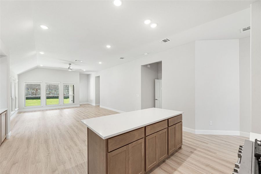 Kitchen island with white countertop and wood cabinets open to living area with vaulted ceiling and light wood floors Kitchen island with white countertop and wood cabinets open to living area with vaulted ceiling and light wood floors