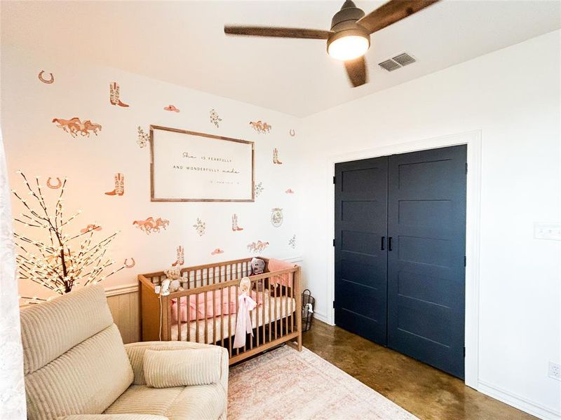 Bedroom featuring finished concrete floors, a crib, a closet, and a ceiling fan Bedroom featuring finished concrete floors, a crib, a closet, and a ceiling fan