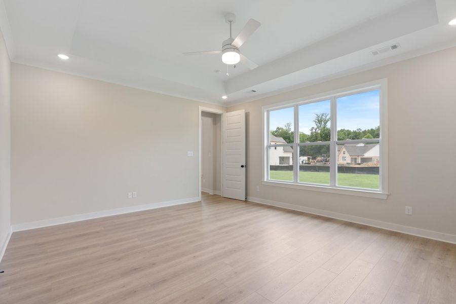 Tray ceiling with a ceiling fan and recessed lighting, light wood-finish flooring, and a large multi-pane window Tray ceiling with a ceiling fan and recessed lighting, light wood-finish flooring, and a large multi-pane window