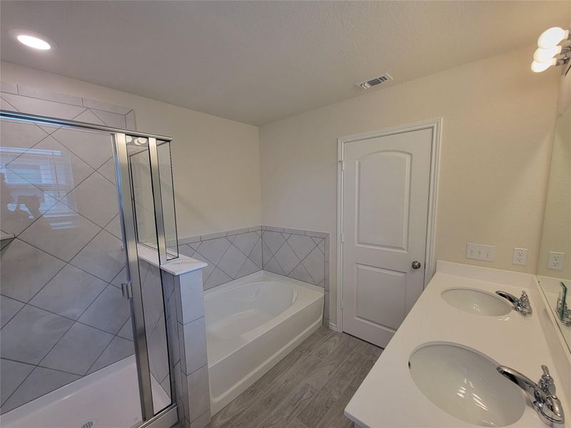Full bath featuring light wood finished floors, a garden tub, double vanity, and a stall shower