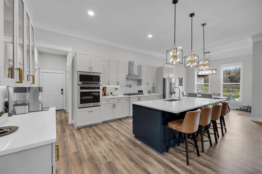 Kitchen with appliances with stainless steel finishes, an island with sink, white cabinetry, and wall chimney range hood