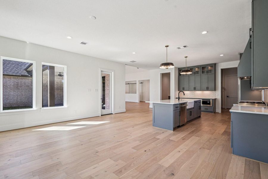 This modern open-concept kitchen and living space features light wood flooring, large windows for natural light, and contemporary gray cabinetry with stainless steel appliances. The kitchen island provides additional workspace and seating, perfect for entertaining.