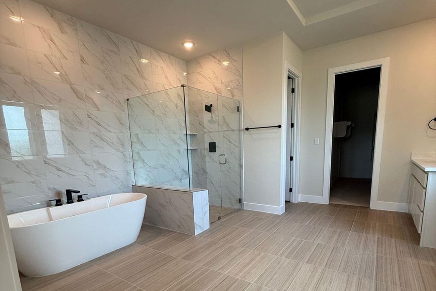Modern bathroom featuring a freestanding soaking tub, glass-enclosed shower, large format marble-look wall tiling, and light wood-finish flooring