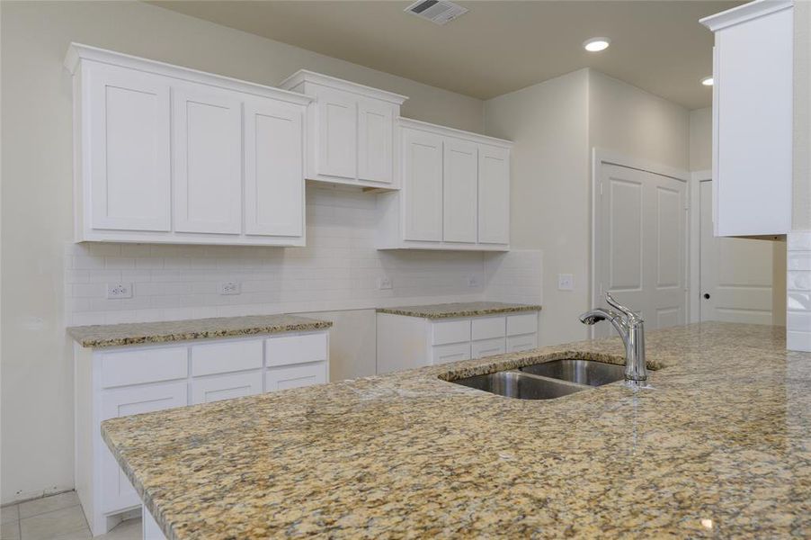 Kitchen featuring decorative backsplash, light stone counters, white cabinetry, and sink