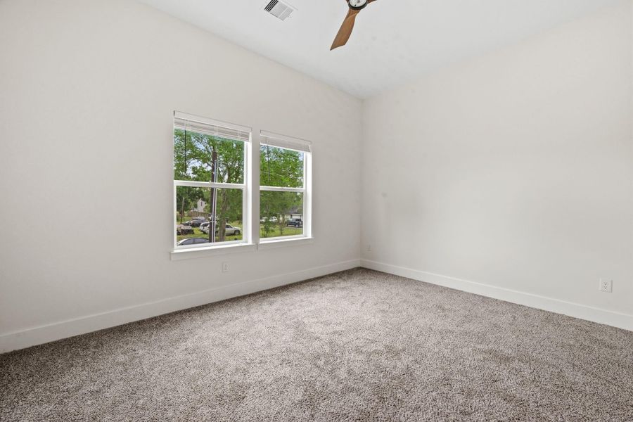 Bright and spacious room with plush carpet, neutral walls, and dual windows offering a view of the outdoors.