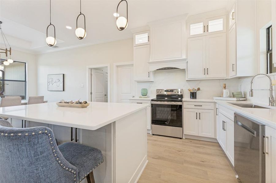 Contemporary kitchen featuring an island with a light-toned countertop, white cabinetry, stainless steel appliances, and wood-finish flooring
