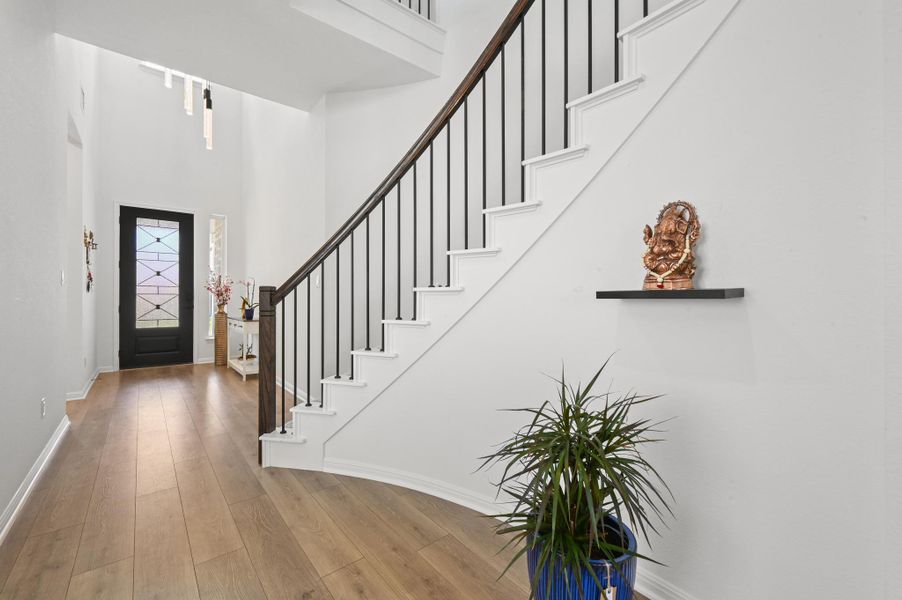 An elegant staircase with modern balusters rises from a wood-floored entryway.