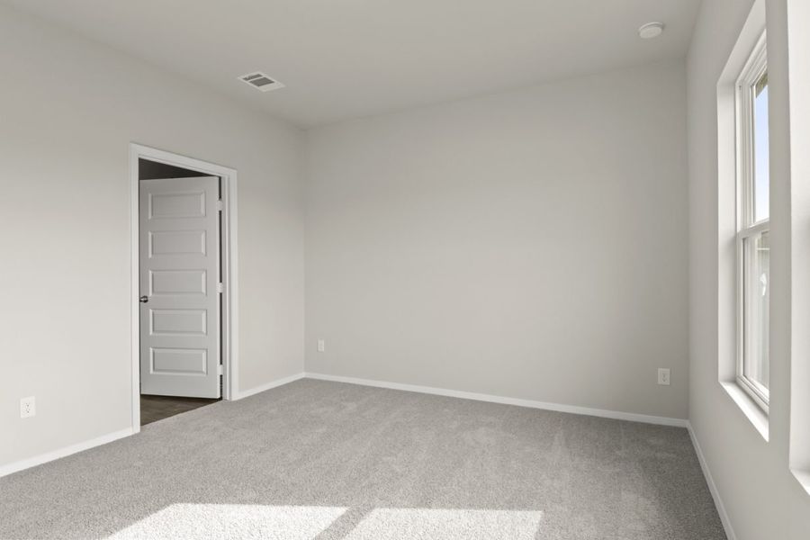 Image of primary bedroom with tan carpet and light grey walls with white door