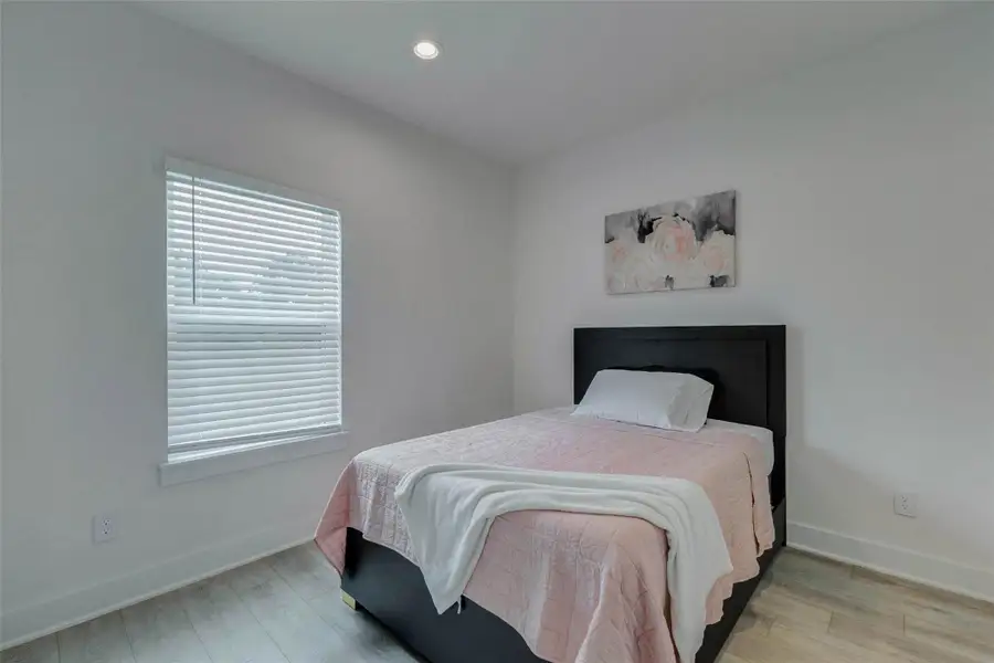 Bright secondary bedroom with neutral walls, wood-look flooring, window blinds, recessed lighting, and a clean, simple layout. The room feels fresh and flexible, offering comfortable space for a guest room, additional bedroom, home office, or private retreat.