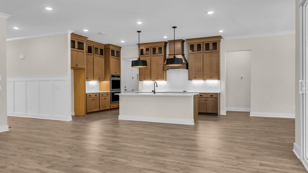 Kitchen with wood colored cabinetry and nearby gathering room (Representative of completed home)