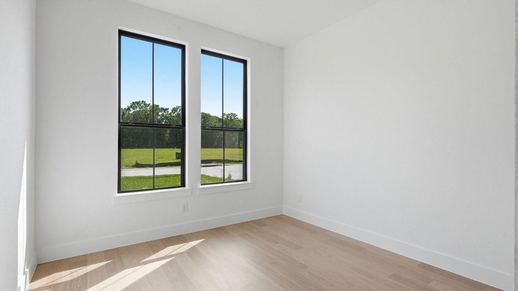 A secondary bedroom with two large windows, neutral painted walls, and wood flooring.