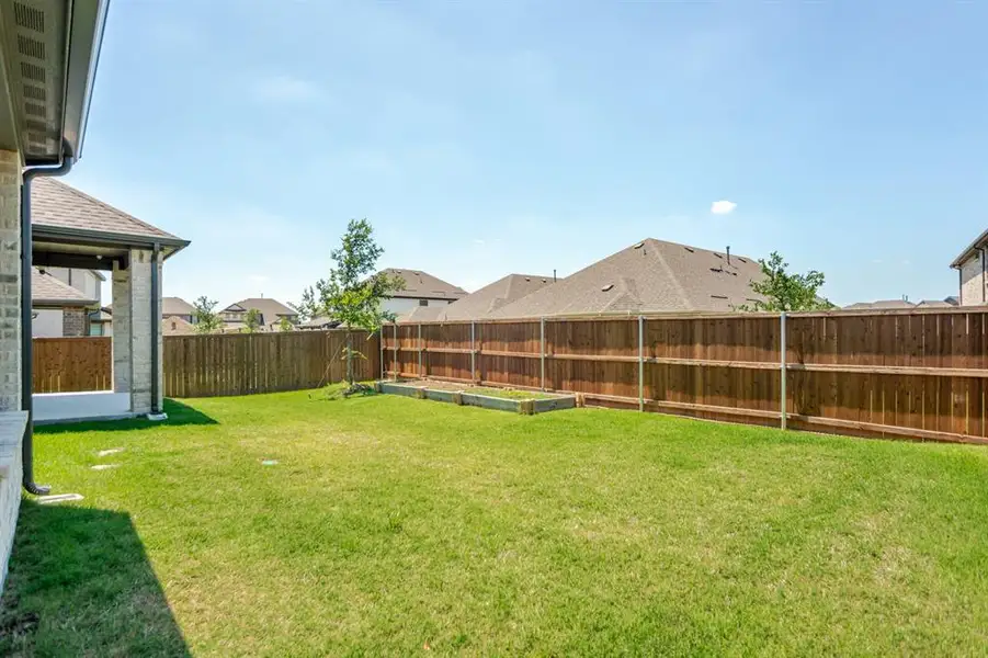 Spacious backyard featuring a covered patio with brick and stone exterior, a full wood privacy fence, and a raised garden bed