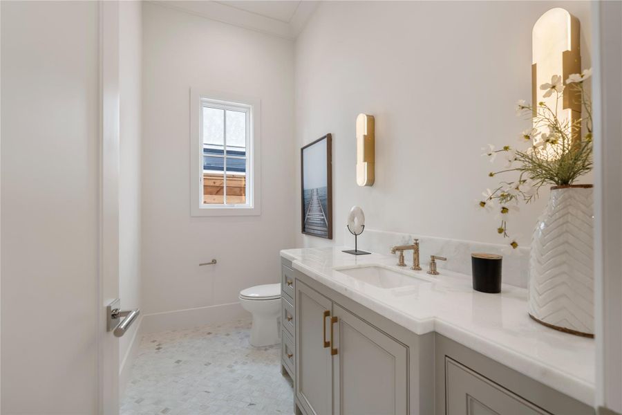 The first floor powder bath, replete with marble countertops and flooring, gold Brizo fixtures, and marble sconces. A small window brightens the space while maintaining privacy. The sink is nestled between custom built-ins, offering a sea of storage space. (mirror to be installed)
